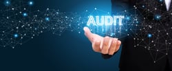  The word 'audit' hovering over a hand, showing benefits of continual RPA audits over manual audits. 