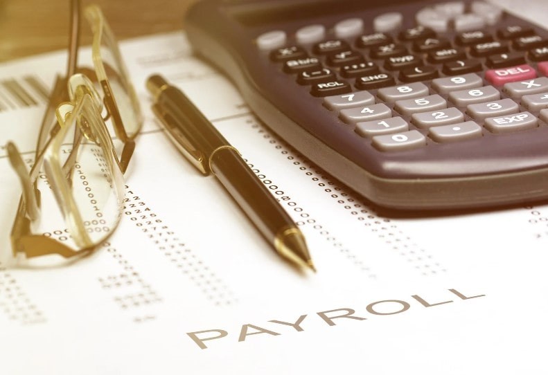 A piece of paper displaying details of payroll alongside a pair of glasses a pen and a calculator